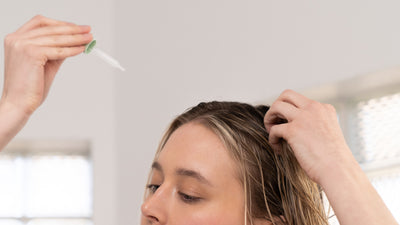 A white lady holding a dropper filled with hair serum above her head